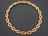 a gold necklace with a braid design on a black background