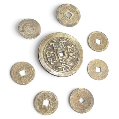 Plusieurs vieilles pièces chinoises sont disposées en cercle sur une surface blanche.