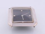 une montre argentée au cadran noir posée sur une surface blanche