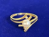 une bague en or sertie d'une perle et de diamants sur un fond bleu