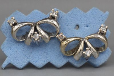 deux paires de boucles d'oreilles en forme de nœud, en argent et diamants, posées sur un morceau de tissu bleu
