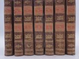 six old books are lined up in a row on a white surface