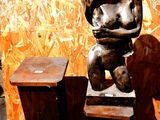 une statue représentant une femme assise sur deux tabourets en bois