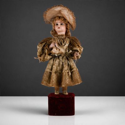 une poupée ancienne représentant une femme vêtue d'une robe dorée et d'un chapeau