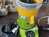 une centrifugeuse jaune et verte posée sur une table en bois, à côté d'autres objets