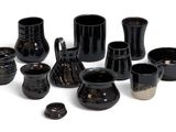 many black vases and cups sitting on a white surface