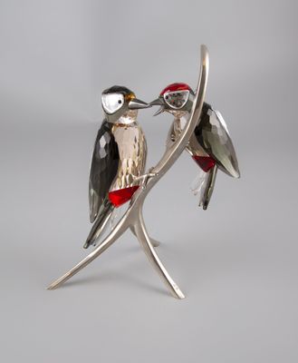 figurine d'oiseau plaquée argent, aux plumes rouges et noires, posée sur une branche