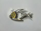 a close up of a fish shaped broochle on a white surface