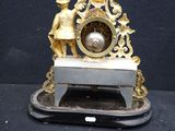 a gold clock on a black table with a key in front of it