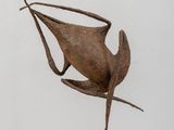 sculpture représentant un oiseau, posée sur un socle en bois, elle-même posée sur une table