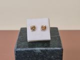 a pair of gold earrings sitting on top of a marble block