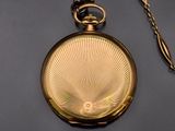 a gold pocket watch with a chain on a gray surface