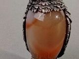une figurine de chouette sur laquelle est posée une pierre orange, entre ses pattes