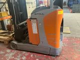 an orange and grey forklift sitting in a warehouse next to a pallet