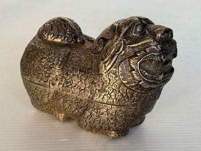 une figurine de chien en argent posée sur une surface blanche