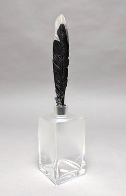 a black feather on top of a clear glass container