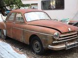 rusted old car parked in front of a trailer in a junkyard