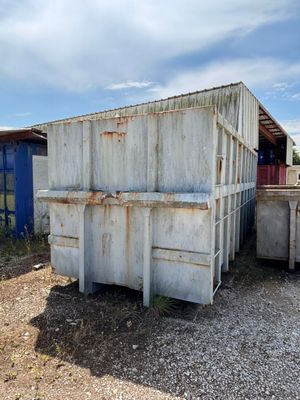 une benne à ordures posée au milieu d'un champ en terre battue