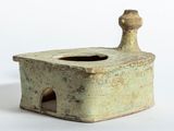 un petit vase vert muni d'une anse en bois, posé sur une surface blanche