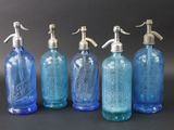 quatre bouteilles en verre bleu avec des bouchons en argent et un bec verseur en argent