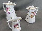 two white porcelain pitchers with floral designs on them sitting on a gray surface