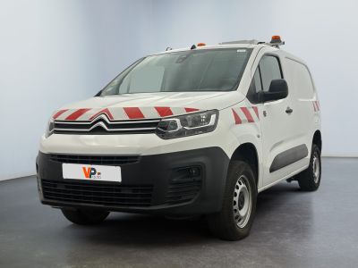 La camionnette blanche est garée dans une grande pièce ; elle porte une bande rouge et blanche sur le côté.