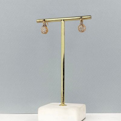 une paire de boucles d'oreilles en or posée sur un socle en marbre, sur fond gris