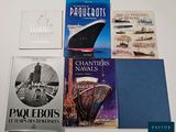 several books on a table with a boat in the background