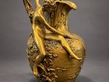 an antique gold vase with a woman sitting on top of it