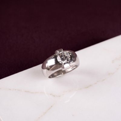 une bague en argent sertie d'un diamant, posée sur une surface en marbre
