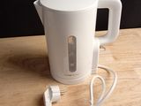 une bouilloire électrique blanche posée sur une table, à côté d'un chargeur