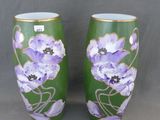 une paire de vases verts ornés de fleurs violettes, posés sur un fond gris