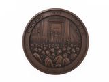 une image représentant une médaille de bronze sur laquelle figure un homme s'adressant à un groupe de personnes