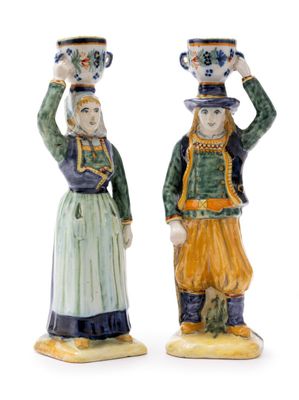 pair of ceramic figurines of a man and a woman with cups on their heads