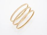 une pile de trois bracelets rigides en or et diamants sur fond blanc
