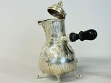une cafetière en argent posée sur un support, avec une poignée noire