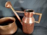 a copper watering can and a copper pot on a black background