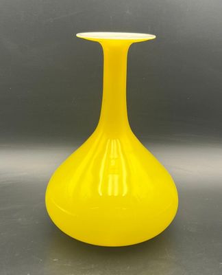 yellow glass vase sitting on top of a table on a gray surface