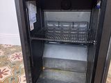 un petit réfrigérateur noir dont la porte est ouverte, posé sur un sol carrelé