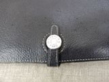 the back of a black purse with a silver button on it
