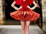the woman is walking down the runway wearing a red dress