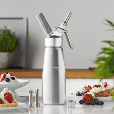 un moulin à poivre en argent posé sur un plan de travail, à côté d'une assiette de fruits