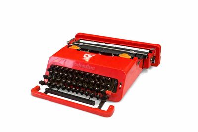 une vieille machine à écrire rouge posée sur un plan de travail blanc