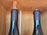 two bottles of wine sitting on a wooden shelf