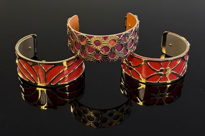 deux bracelets à manchette rouges et dorés posés sur une surface noire