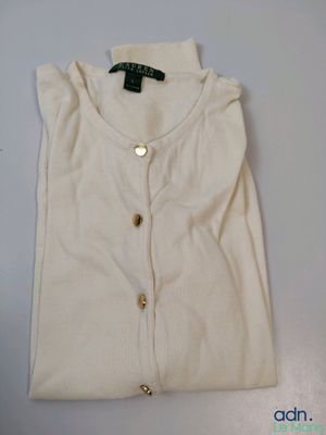 La chemise est blanche, avec des boutons dorés au niveau du col.