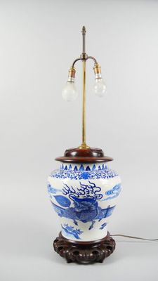 un vase bleu et blanc posé sur un socle sur lequel est posée une lampe