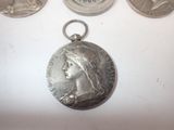 three silver medals are on a white surface next to a coin