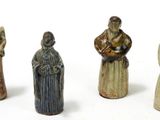 four ceramic figurines of people standing in a line on a white surface