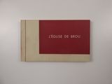 un livre rouge posé sur un mur blanc, à côté d'un mur blanc